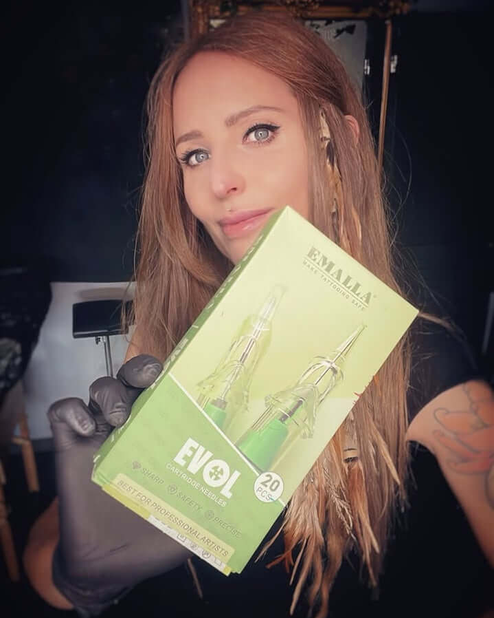 Tattoo artist holding EMALLA EVOL tattoo cartridge needles box for professional tattooing